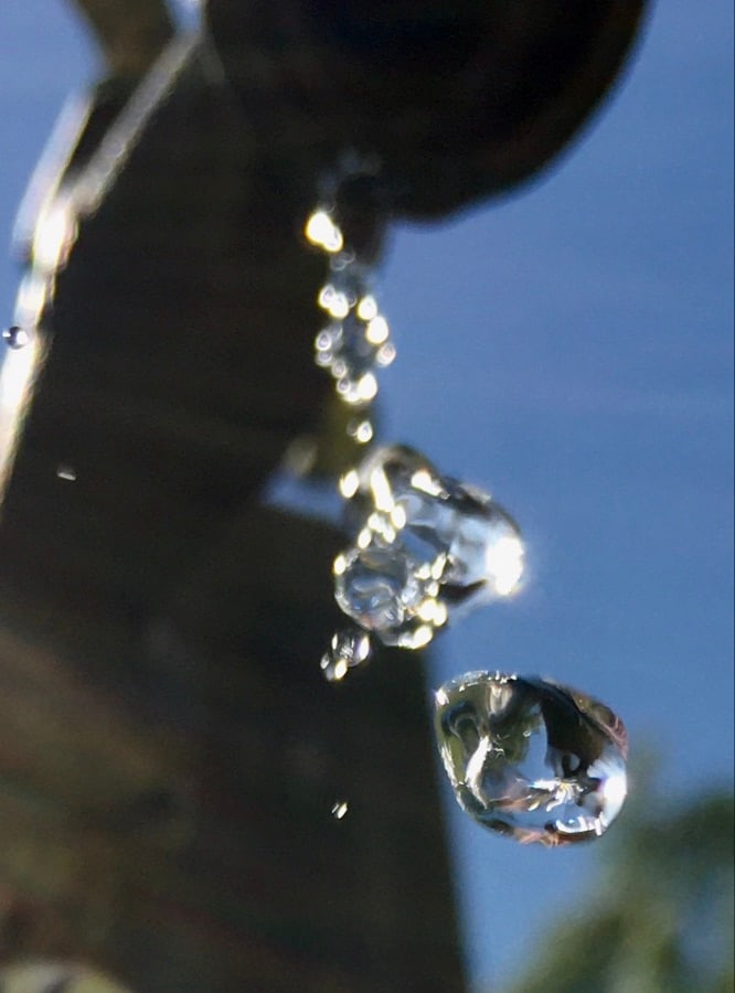 Macro view of water droplets falling from a spout or pipe against a bright blue sky