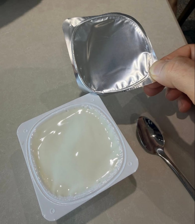 A sealed cup of smooth white dessert or yogurt opened with a spoon beside it at Lily Dim Sum