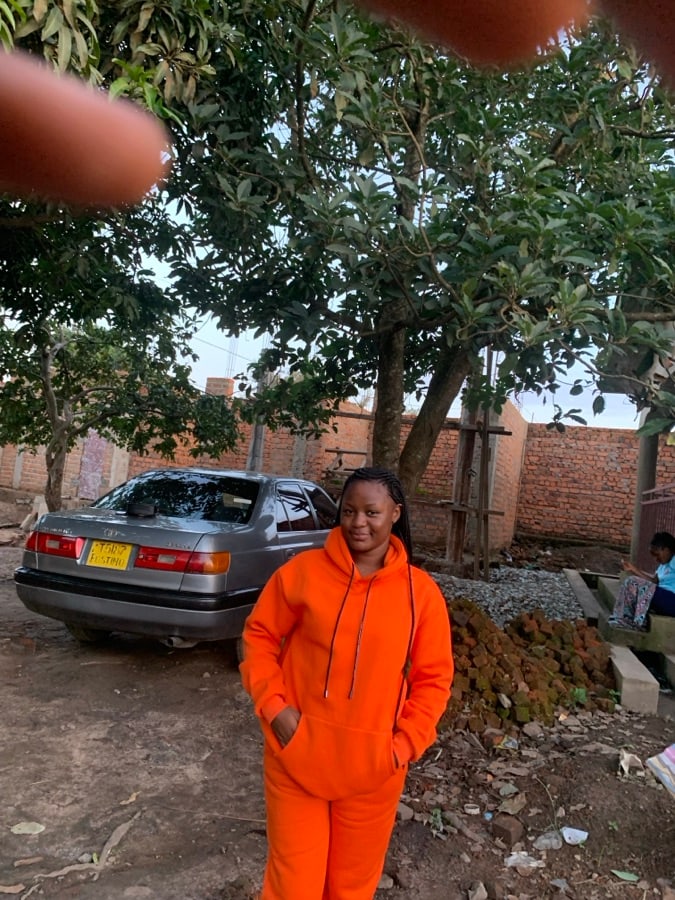 Portrait d’une personne en survêtement orange vif, debout en extérieur sous les arbres