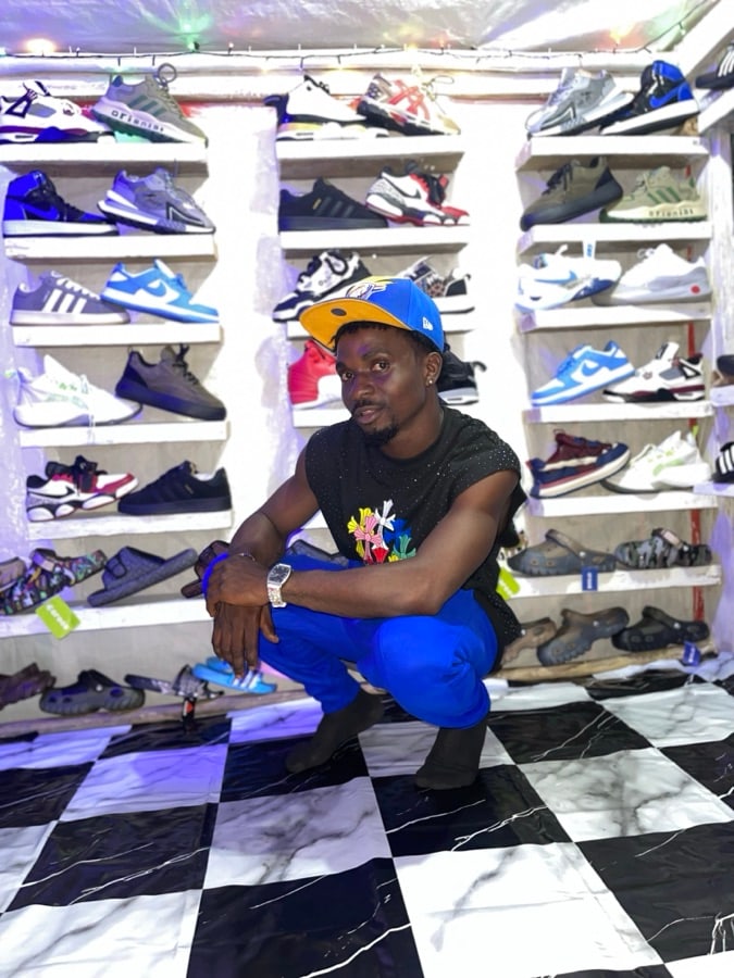 Man posing inside a shoe shop with many sneakers displayed on wall shelves