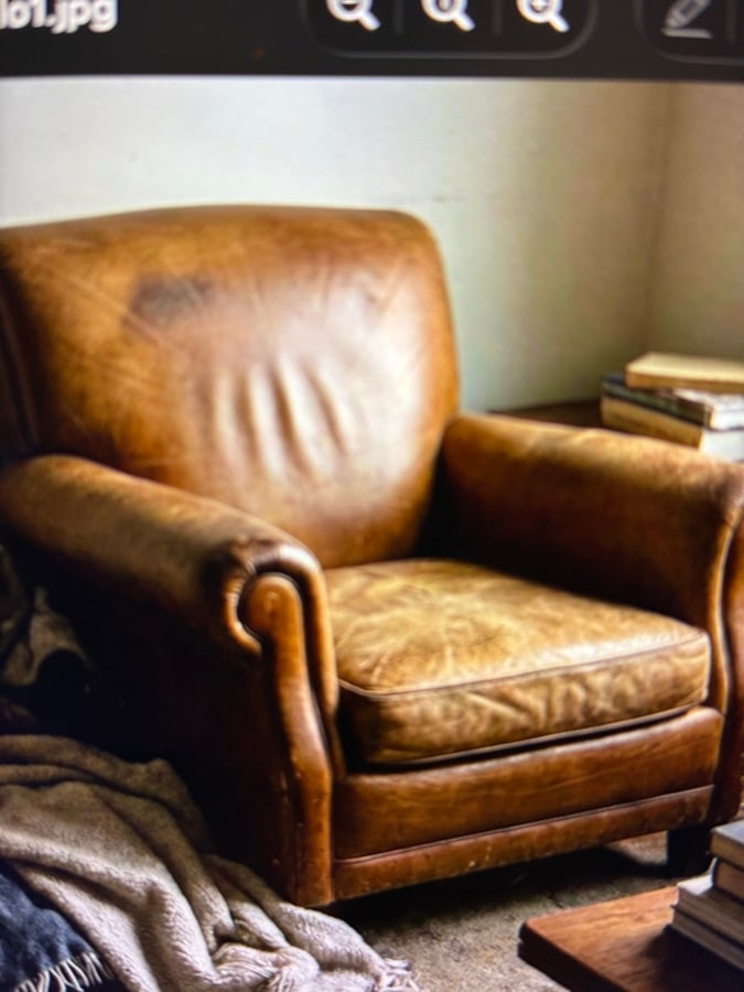 Classic brown leather armchair beside stacked books and a soft throw
