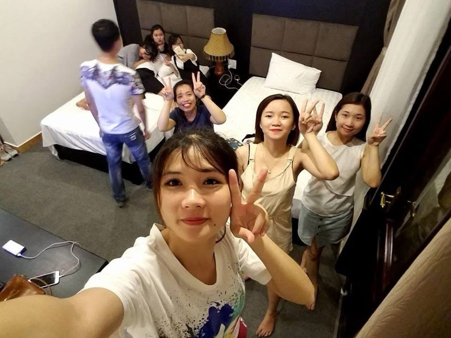 Group selfie of young friends smiling and making peace signs inside a room with beds